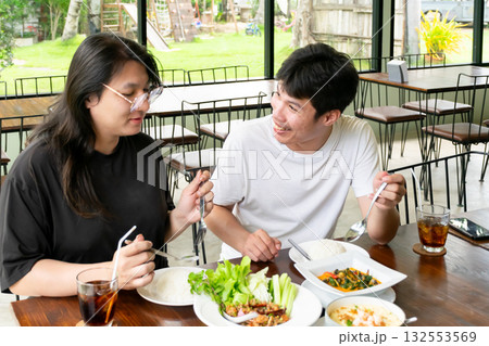 Two Thai LGBTQ friends enjoying lunch laughing and talking together in a cozy cafe with warm daylight atmosphere showing real friendship happiness and everyday life connection 132553569