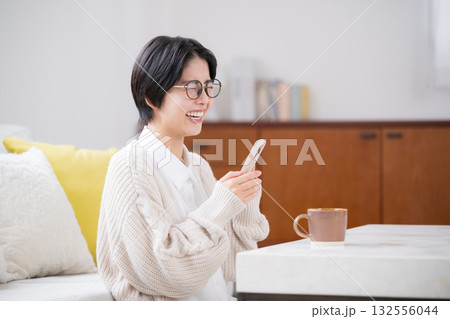 部屋でニットを着てスマホを見て大笑いする笑顔のかわいい女性 部屋でニットを着てスマホを見て大笑いする笑顔のかわいい女性 132556044