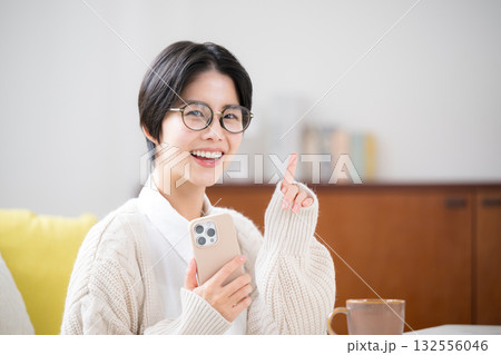 部屋でニットを着てスマホをタップ、見るショートカットの女性 萌袖で指差しのポイント 部屋でニットを着てスマホをタップ、見るショートカットの女性 萌袖で指差しのポイント 132556046