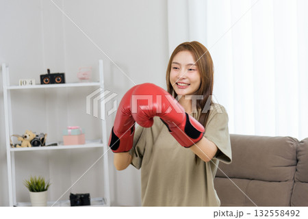 Young happy woman enjoys activity at home, engaging in fitness training workout, wearing red boxing gloves, people embracing active lifestyle, finding joy in personal exercise 132558492