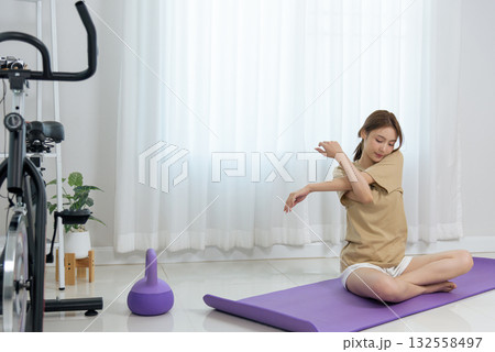 Young woman stretching arm, engaging in home activity on yoga mat, practicing gentle exercise, promoting healthy people lifestyle, happy and focused for wellness Young woman stretching arm, engaging in home activity on yoga mat, practicing gentle exercise, promoting healthy people lifestyle, happy and focused for wellness 132558497