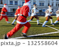 Santa Claus is jogging on a vibrant green field before a football match takes place on Christmas Eve, filled with excitement and holiday energy. 132558604
