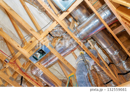 Workers install ventilation ducts between wooden beams in home under construction, utilizing tools ladders. Workers install ventilation ducts between wooden beams in home under construction, utilizing tools ladders. 132559081