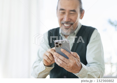 笑顔でスマートフォンを操作する70代の男性の手元 132560802