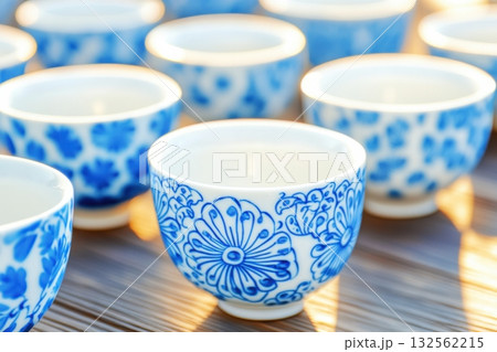 Intricate blue porcelain tea cups arranged on a wooden table reflecting warm golden light Intricate blue porcelain tea cups arranged on a wooden table reflecting warm golden light 132562215