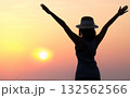 The silhouette of a dreamy girl looking up at the horizon. woman watching the sunset by the sea Raise your hand to welcome the fresh air in the evening. 132562566