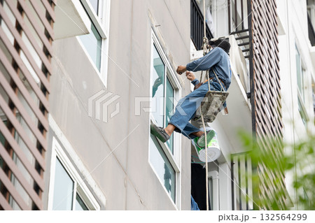 Exterior repair worker rappel down using ropes to repair leaking cement walls residential buildings. Exterior repair worker rappel down using ropes to repair leaking cement walls residential buildings. 132564299