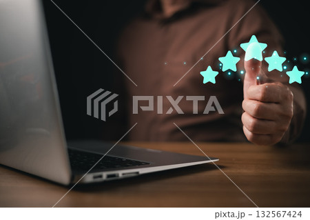 A man in a brown shirt gives a glowing thumbs up near a laptop, with five illuminated stars representing high satisfaction, quality, and positive customer service feedback in a digital context. 132567424