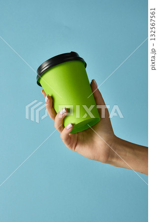 Hand holding green takeaway coffee cup with black lid on blue background for product marketing 132567561
