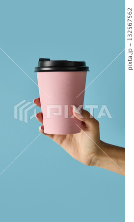 Hand holding pink takeaway coffee cup with black lid on blue background for cafe branding Hand holding pink takeaway coffee cup with black lid on blue background for cafe branding 132567562