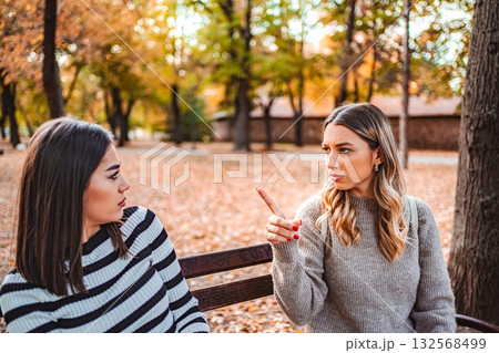 Two girls share a heartfelt conversation in a colorful autumn park 132568499