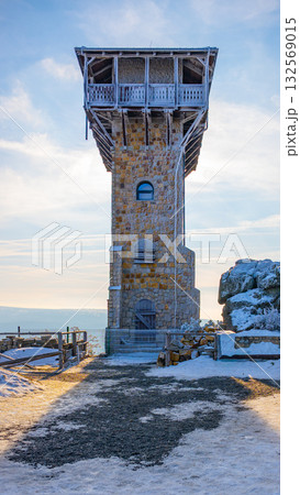 A stone lookout tower stands proudly on Wysoki Kamien in Poland's Jizera Mountains. The structure showcases its unique architecture against a serene sky, surrounded by snowy ground. 132569015