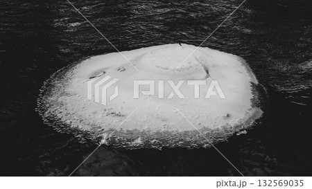 A serene winter scene of a frozen section of the Jizerka River. The icy surface contrasts with the flowing water, showcasing nature's beauty during cold months in the Czech landscape. 132569035