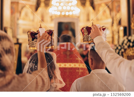 Wedding crowns held over newlyweds during Orthodox ceremony, back view 132569200