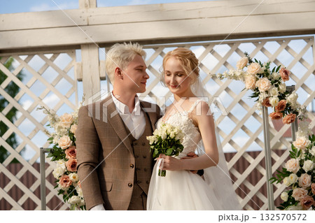 Couple exchanges vows at an outdoor wedding ceremony under a floral arch 132570572