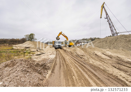 Heavy machinery like dump trucks and excavators operate in a construction area, moving earth and preparing for new road developments under cloudy skies Heavy machinery like dump trucks and excavators operate in a construction area, moving earth and preparing for new road developments under cloudy skies 132571233
