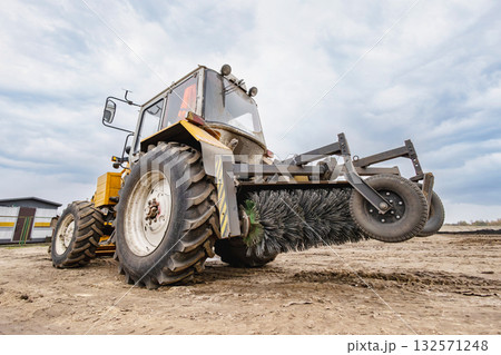 A tractor uses a brush attachment to clear mud and debris from a farm field, showcasing the machinery's function in agricultural maintenance A tractor uses a brush attachment to clear mud and debris from a farm field, showcasing the machinery's function in agricultural maintenance 132571248