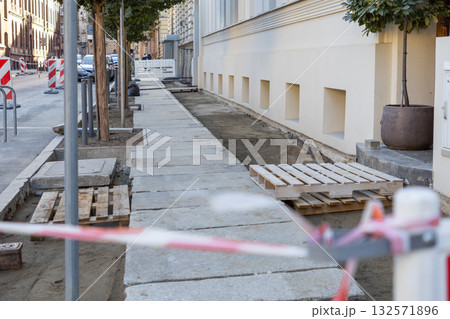 Sidewalk under reconstruction with new concrete paving stones, wooden pallets, and barrier tape, representing urban infrastructure development and city maintenance Sidewalk under reconstruction with new concrete paving stones, wooden pallets, and barrier tape, representing urban infrastructure development and city maintenance 132571896