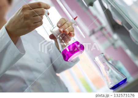 Close-up of a scientist pipetting during a titration with pink indicator in a flask, perfect for chemistry, education, pharma, biotech and R and D uses 132573176