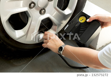 Woman using portable tire inflator with pressure gauge to check and inflate car wheel. Auto maintenance safety concept. 132573272