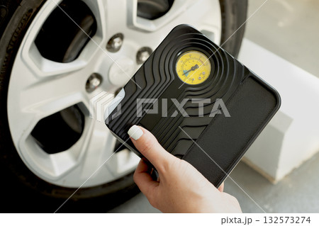 Female hand holding portable tire inflator with built-in pressure gauge near car wheel. Auto care concept. 132573274