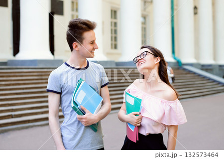 Young students spending time together. Reading book, communicating while standing near stairs of old conventional university in small town 132573464