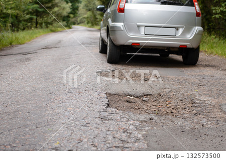Back af a modern car driving olong the countryside road with a lot of potholes Back af a modern car driving olong the countryside road with a lot of potholes 132573500
