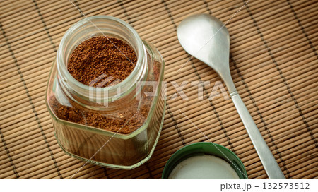 Jar of coffee with cover and a spoon on a brown bamboo background 132573512