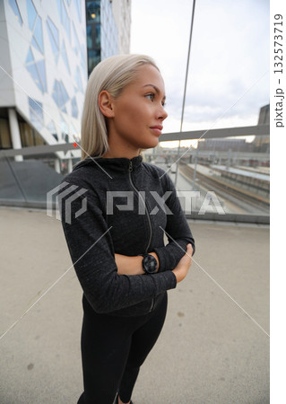 Confident young woman in black activewear standing outdoors near urban buildings Confident young woman in black activewear standing outdoors near urban buildings 132573719