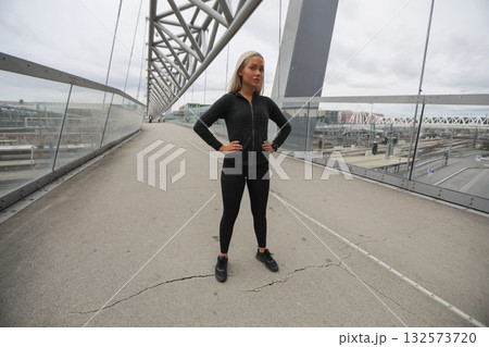 Confident woman in fitness attire on a modern bridge in the city Confident woman in fitness attire on a modern bridge in the city 132573720
