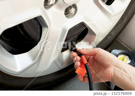 Woman uses portable tire inflator with pressure gauge to check and inflate car tire.Car maintenancet 132576009