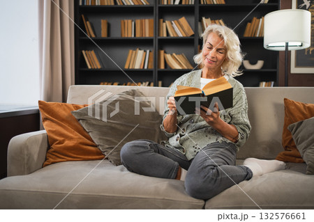 Comfort relaxed senior old elderly woman reading book at home. Mature woman resting enjoy calm day sitting on sofa at home alone. Adult lady spending free time keeping book smiling. Pension concept 132576661