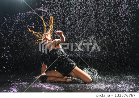 Contemporary woman dancer posing in rain water on black background. Female artist performer dancing with expression. Modern ballerina dancing in darkness. Passion dance in dark. Flexibility balance 132576767