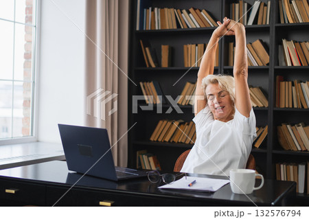 Middle aged senior woman relaxing stretching arms and body taking break from work on laptop at home. Older mature woman happy after work done satisfied by good result. Fatigue from long laptop usage Middle aged senior woman relaxing stretching arms and body taking break from work on laptop at home. Older mature woman happy after work done satisfied by good result. Fatigue from long laptop usage 132576794