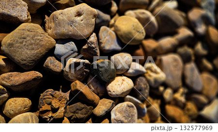 texture of a natural assortment of pebbles and river stones in warm earth tones, ideal for landscaping, garden borders, pathways, or decorative rock surfaces 132577969
