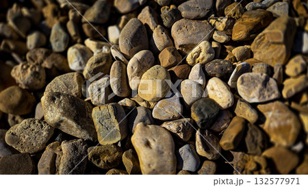 texture of a natural assortment of pebbles and river stones in warm earth tones, ideal for landscaping, garden borders, pathways, or decorative rock surfaces 132577971