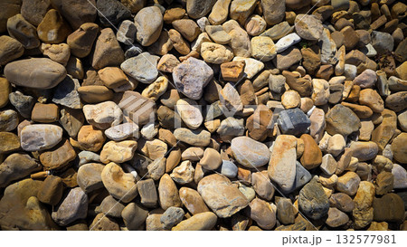 texture of a natural assortment of pebbles and river stones in warm earth tones, ideal for landscaping, garden borders, pathways, or decorative rock surfaces 132577981
