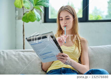 Young student girl study online, sitting at home on couch with textbook 132578880