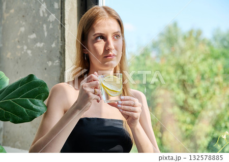 Young beautiful blonde woman with glass of lemon water at home 132578885