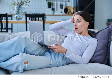 Surprised teenage girl looking at laptop, lying on sofa at home 132578893