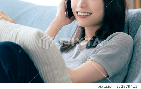 ソファに座ってスマートフォンで話す笑顔の女性 132579413