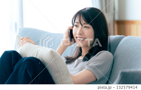 ソファに座ってスマートフォンで話す笑顔の女性 ソファに座ってスマートフォンで話す笑顔の女性 132579414