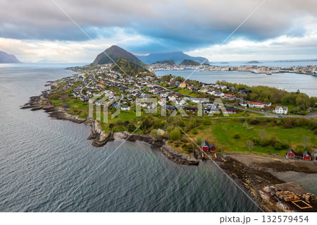 Alesund waterfront with traditional Nordic architecture, peaceful harbor, and lush mountain backdrop in soft daylight. 132579454