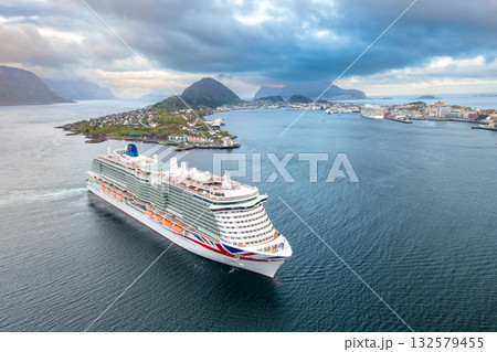 Impressive cruise ship navigates clear waters near mountainous coastline of Alesund town. Cloudy sky adds dramatic touch to serene Nordic vista Impressive cruise ship navigates clear waters near mountainous coastline of Alesund town. Cloudy sky adds dramatic touch to serene Nordic vista 132579455