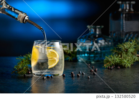 Gin is poured from a bottle into a glass with ice and lemon slice. 132580520