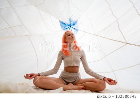 Young Woman Meditating in a White Tent With a Blue Umbrella Overhead 132580545