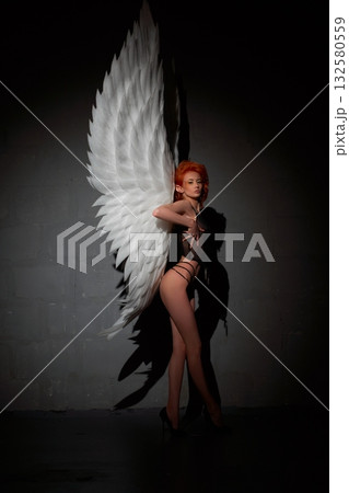 Confident woman with big feather wings standing in the darkness Confident woman with big feather wings standing in the darkness 132580559