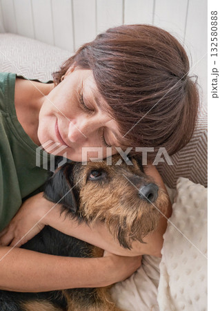 Caucasian mature female relaxing with dog on sofa at home. Caucasian mature female relaxing with dog on sofa at home. 132580888
