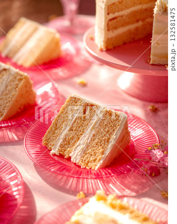 Close-up of a delicious layer cake slice with white buttercream frosting on a vibrant pink glass plate. 132581475
