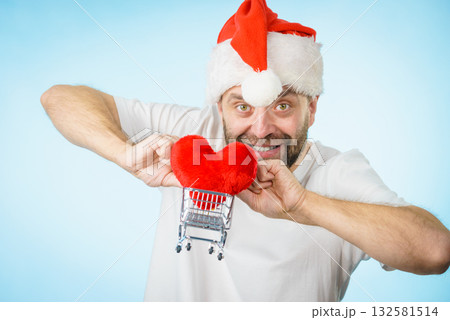 Man in santa hat holds shopping cart with heart. Man in santa hat holds shopping cart with heart. 132581514